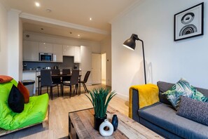 A modern living room with a sofa, a coffee table, and a dining area with chairs and a kitchen in the background. - Brighton Blissful Retreat by the Sea (Brighton)