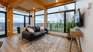 Una sala de estar moderna con un sofá de cuero negro, una mesa de centro de madera y ventanas amplias con vistas a las montañas.