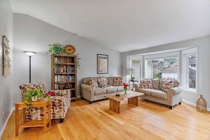 A living room with a sofa, armchair, coffee table, bookshelf, and a large window. - Large Family-Friendly Home on NW Side - Dogs OK (Olympia)