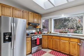 A kitchen with wooden cabinets, stainless steel appliances, a water dispenser, and a window with a view of trees. - Large Family-Friendly Home on NW Side - Dogs OK (Olympia)