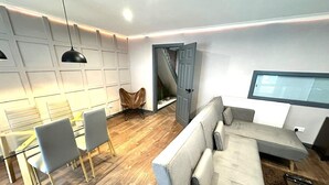 Ein modernes Wohnzimmer mit einer Couch, Sesseln, einem Esstisch und einem Fernseher.