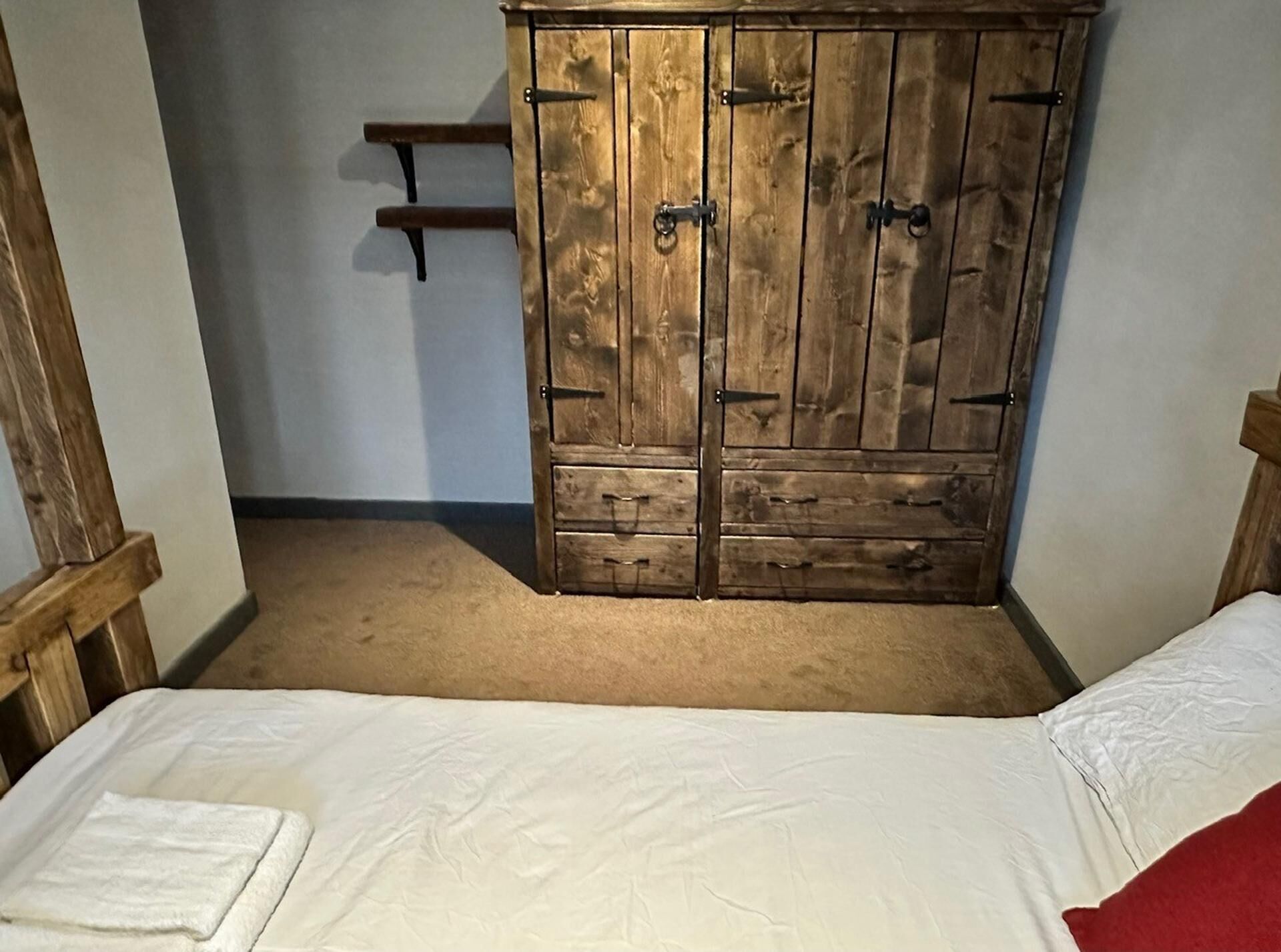 A bedroom with a wooden wardrobe, a bed with white bedding, and a red pillow.