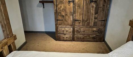 A bedroom with a wooden wardrobe, a bed with white bedding, and a red pillow.