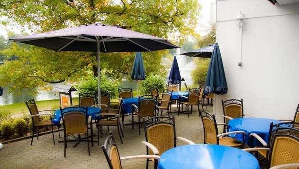 Un espace extérieur aménagé en terrasse, avec des tables et des chaises, protégé par des parasols, et offrant une vue sur un lac.