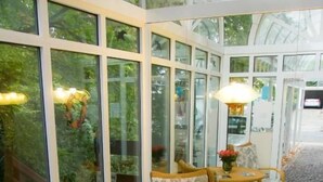 Une véranda meublée de mobilier en osier, une table centrale décorée de fleurs et de grandes portes vitrées.