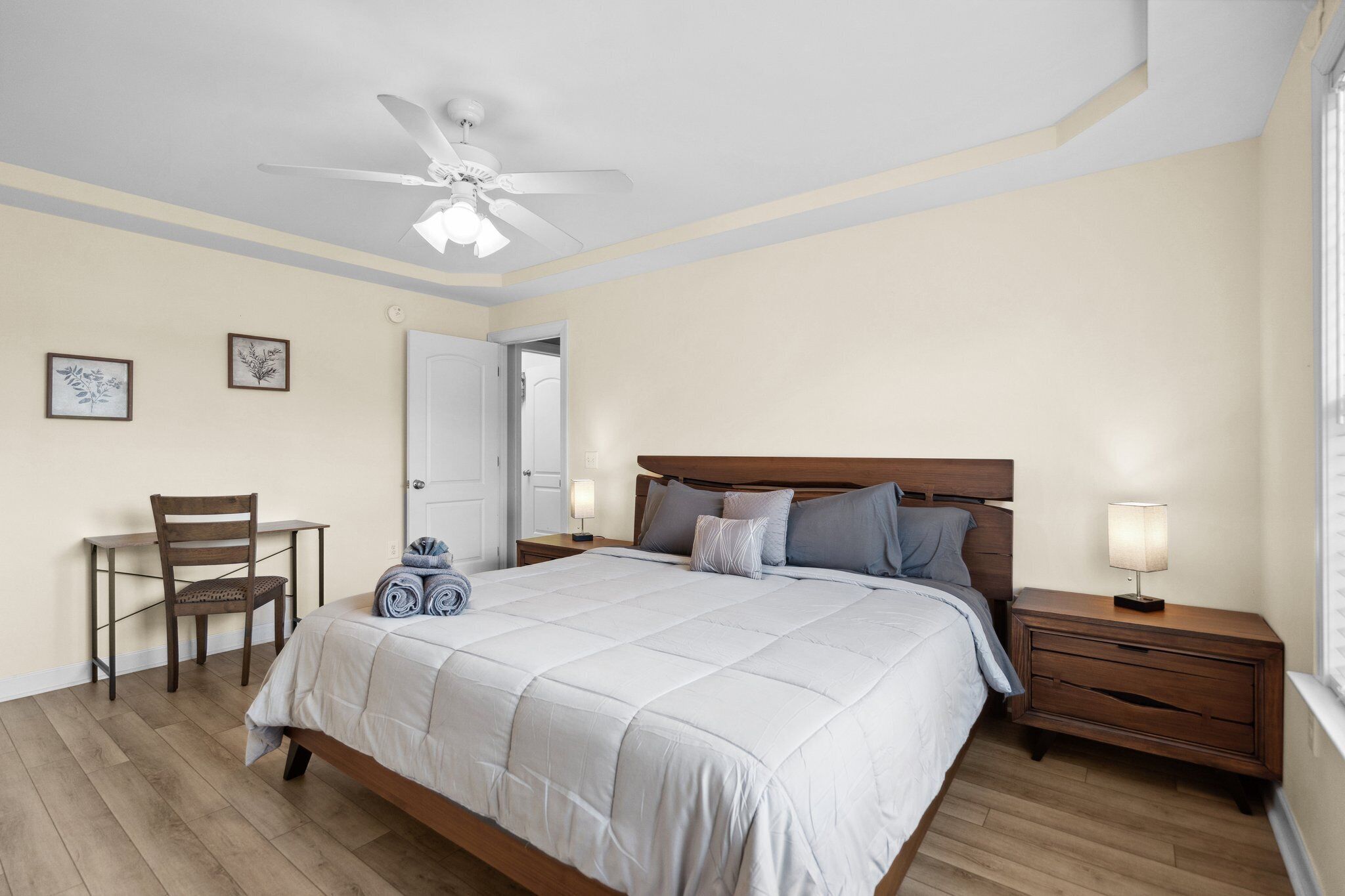 Ein Schlafzimmer mit Bett, Schreibtisch, Stuhl, Nachttisch und Deckenventilator.