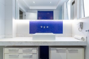 A modern bathroom with a white sink, blue mosaic tiles, and a white countertop.