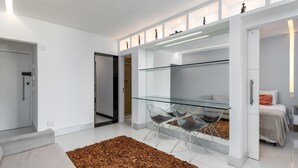 Un interior moderno con una mesa de comedor de vidrio, un sofá y una cama con cabecera blanca.