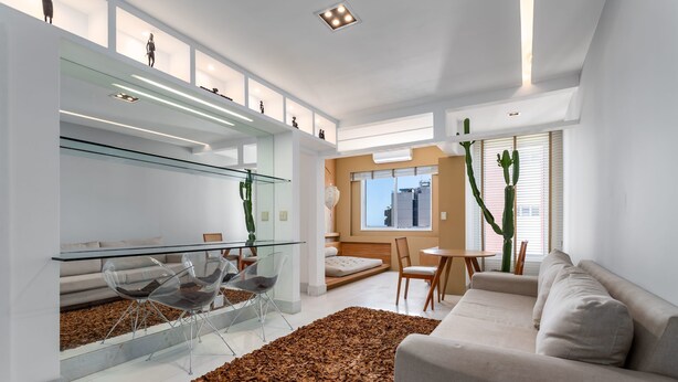 Una sala moderna con una mesa de comedor de vidrio, sillas traslúcidas, un sofá color beige y un tapete marrón grande.