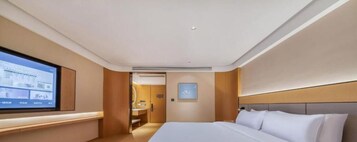 A hotel room with a large bed, a flat-screen TV mounted on the wall, and a wooden headboard.