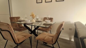 A dining area with a glass-top table, four cushioned chairs, white dinnerware, and wine glasses. - Modern City Apartment (Hemel Hempstead)