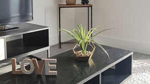 A modern living room with a black coffee table, a flat-screen TV, a clock, a plant, and a framed artwork on the wall. - Modern City Apartment (Hemel Hempstead)