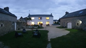 Une cour bordée de bâtiments en pierre, un chemin pavé et des espaces de repos en plein air.