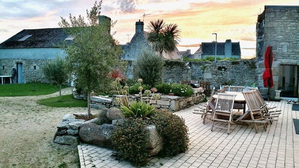 Une cour bordée de bâtiments en pierre, une terrasse dallée et des meubles d’extérieur.