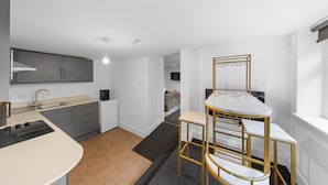 Una habitación moderna y compacta con kitchenette, una cama y un pequeño comedor.