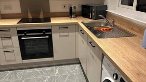 Una cucina compatta con forno integrato, microonde e lavatrice, caratterizzata da un pavimento in marmo e un piano di lavoro in legno.