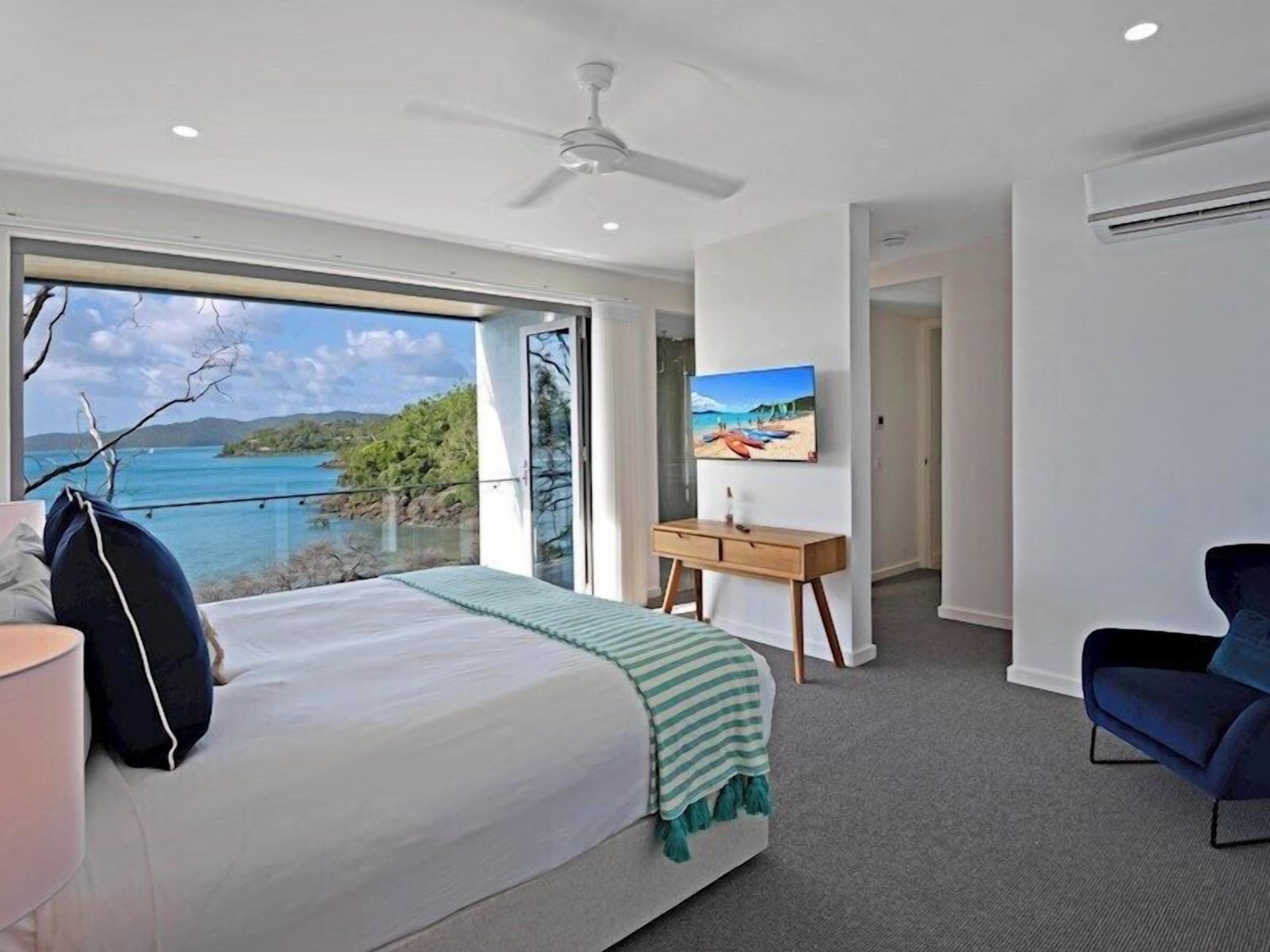 A bedroom with a large bed, a desk, a chair, and a painting.