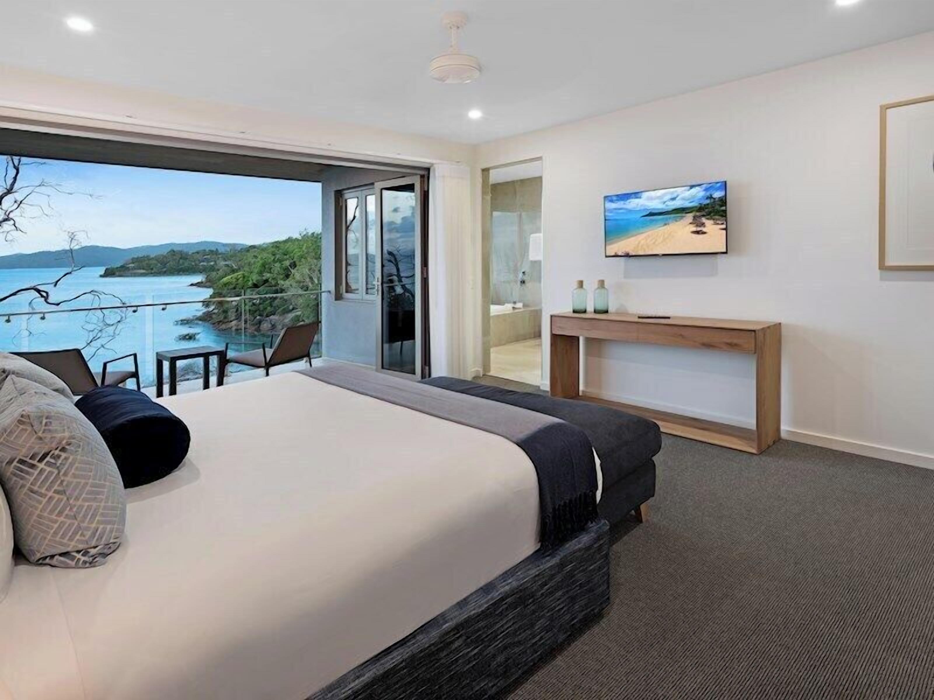 Une chambre avec un grand lit, une vue sur la mer, un balcon et un téléviseur posé sur une console en bois.
