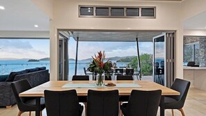A modern dining area with a large table, black chairs, and a view of the sea.