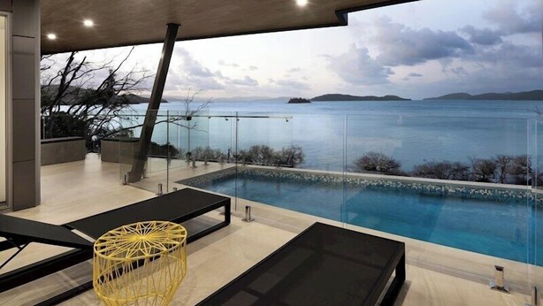 A modern outdoor pool area with a clear view of the sea and distant islands.