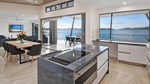 A modern kitchen with a large island, dining area, and a view of the sea.