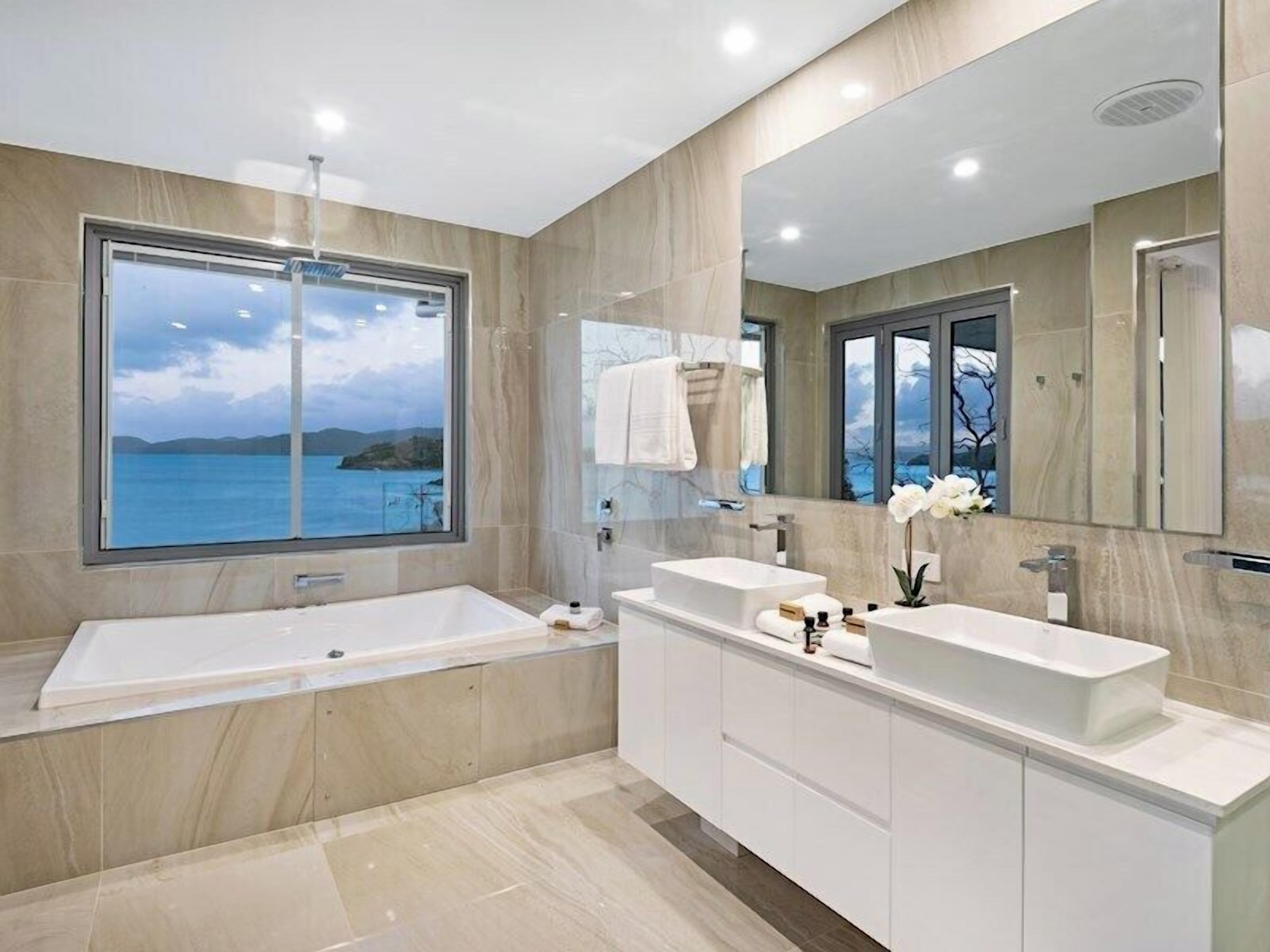 Une salle de bain moderne avec une grande baignoire, deux lavabos et un grand miroir.