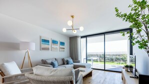 Una sala moderna con un sofá, una mesa de centro y un mueble para televisión. Hay tres cuadros en la pared y una lámpara de pie.