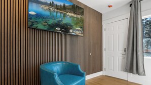 A room with a wooden slat wall, a mounted TV, a blue upholstered chair, and a door with a grey curtain. - Zephyr Cove Unit 2 (Zephyr Cove)