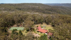 An aerial view of a property with a tennis court, a red-roofed building, and surrounding dense forest. - Balmaghie - charming, secluded 7 acre rural retreat in the Southern Highlands (Bundanoon)
