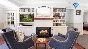 A living room with a fireplace, a television, bookshelves, and two armchairs. - Balmaghie - charming, secluded 7 acre rural retreat in the Southern Highlands (Bundanoon)