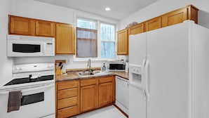 A kitchen with wooden cabinets, a white refrigerator, a stove, a microwave, and a dishwasher. - C.a.l.m. Cottage At The Last Mile 2 Bedroom Home (Savannah)