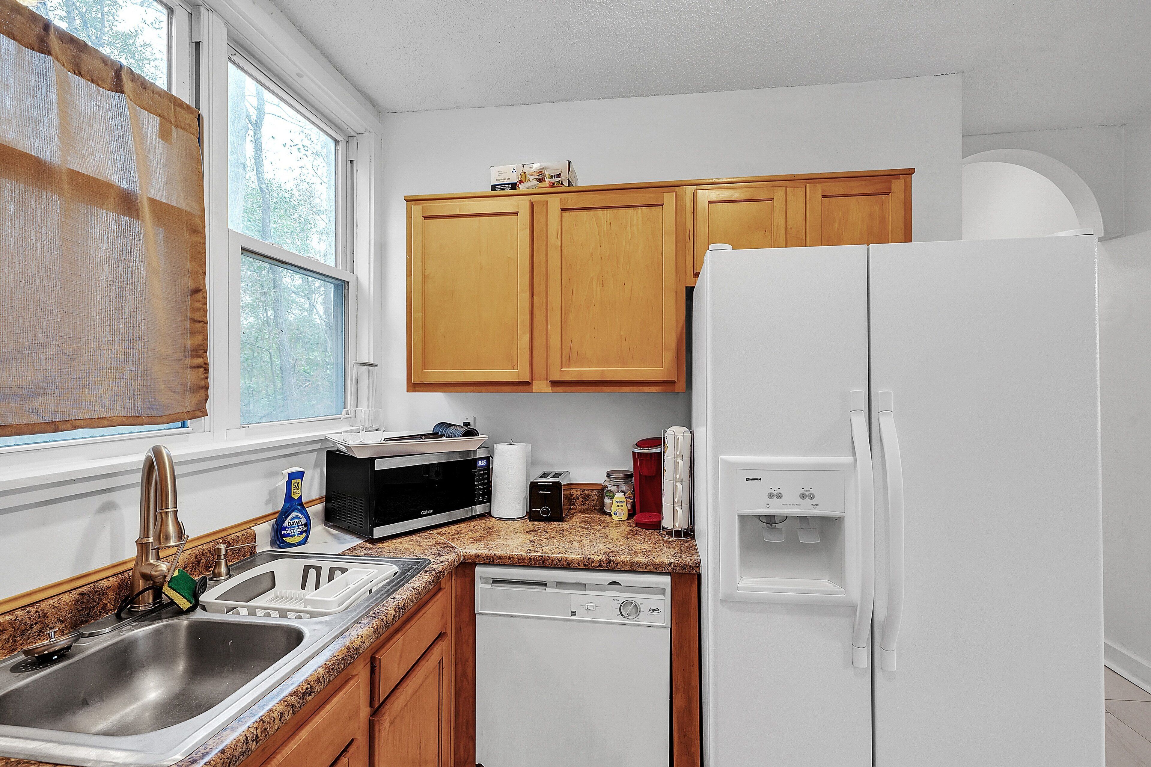 A kitchen with wooden cabinets, a white refrigerator, a microwave, a sink, and a dishwasher.