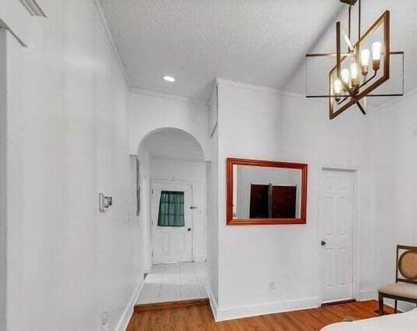 A room with white walls, a wooden floor, a door with a mirror, and a ceiling light fixture. - C.a.l.m. Cottage At The Last Mile 2 Bedroom Home (Savannah)