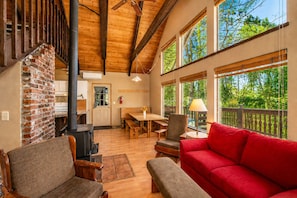 Un intérieur chaleureux avec une cheminée, des meubles en bois et de grandes fenêtres donnant sur un paysage verdoyant.