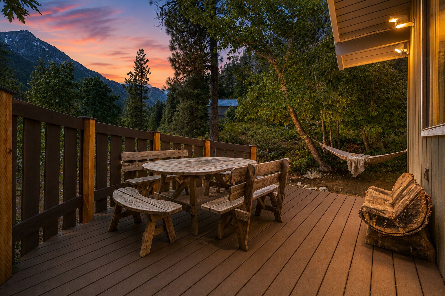 Una terraza de madera con una mesa redonda y bancos, rodeada de árboles y un paisaje de montaña.