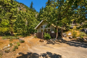 Une cabane dotée d’une terrasse en bois, entourée d’une forêt dense et d’un terrain rocheux.
