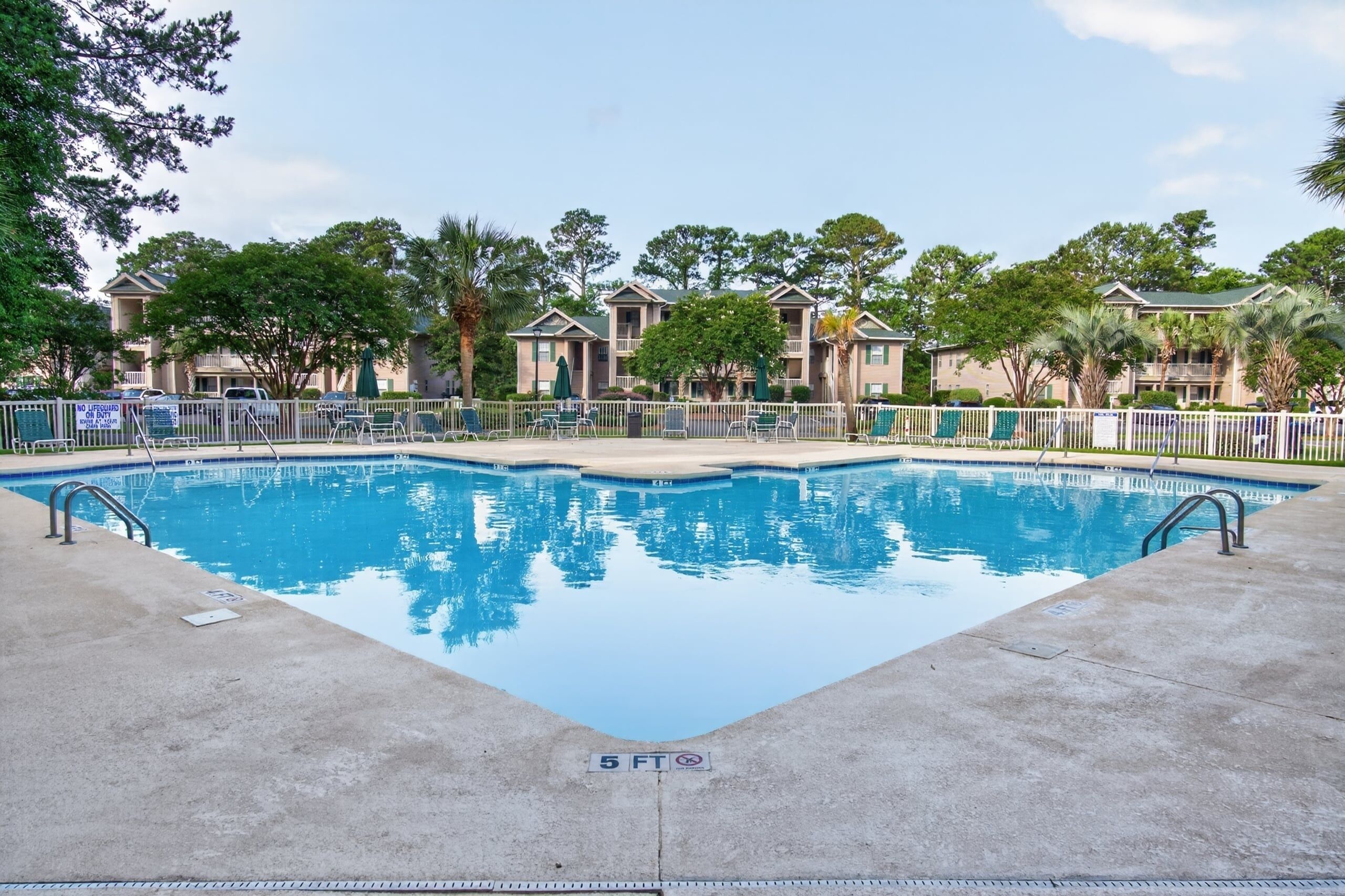 A swimming pool with a 5 ft depth marker, surrounded by a fence, with a building in the background.