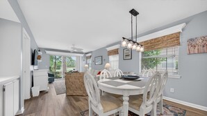 A dining area with a round table, white chairs, and a patterned rug. - 11d True Blue Golf Haven 3 Bedroom Condo (Pawleys Island)