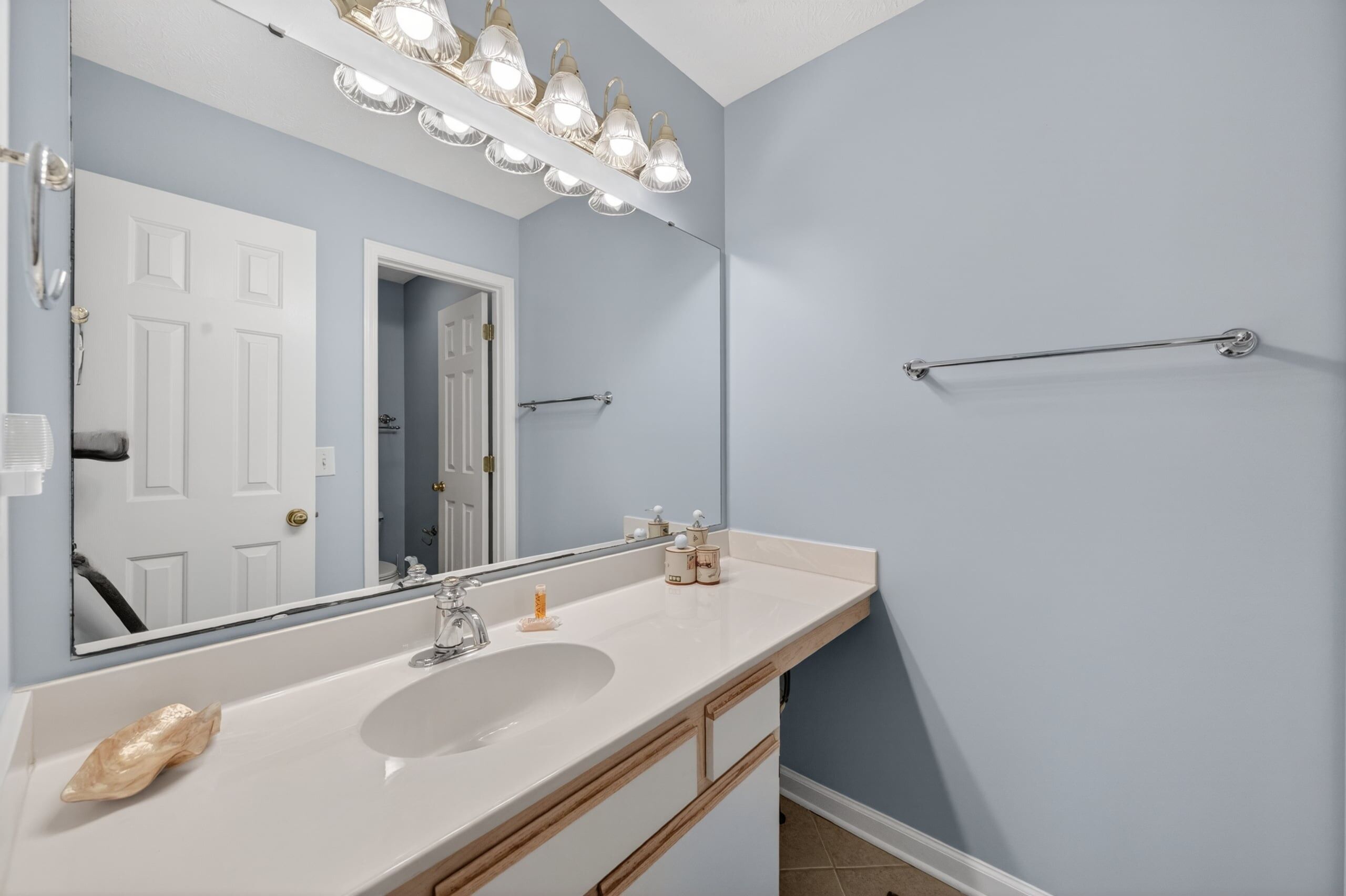 Une salle de bain avec un lavabo blanc, un grand miroir et un porte-serviettes.