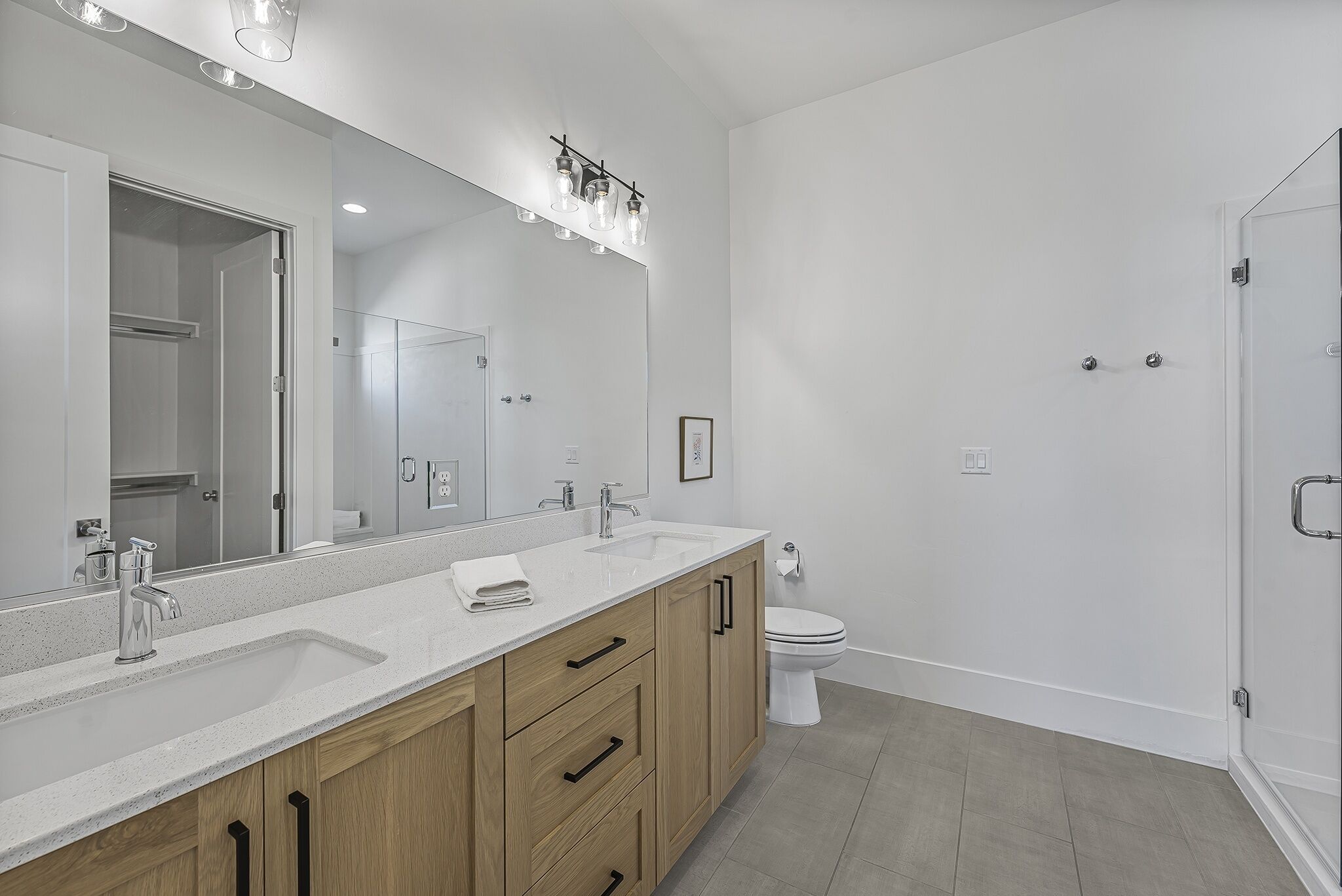 Un baño moderno con un espejo grande, dos lavamanos y un inodoro.