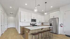 A modern kitchen with white cabinets, a stainless steel refrigerator, a microwave, and a large island with stools. - Villa #35 At Bloomington Country Club 4 Bedroom Townhouse (St. George)