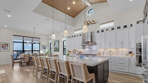 Une cuisine spacieuse avec des meubles blancs, un grand îlot central et des luminaires suspendus.