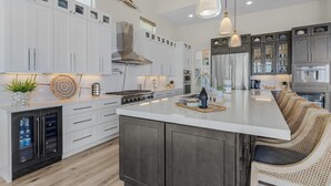 Une cuisine moderne avec des meubles blancs, un grand îlot central et une cave à vin intégrée.