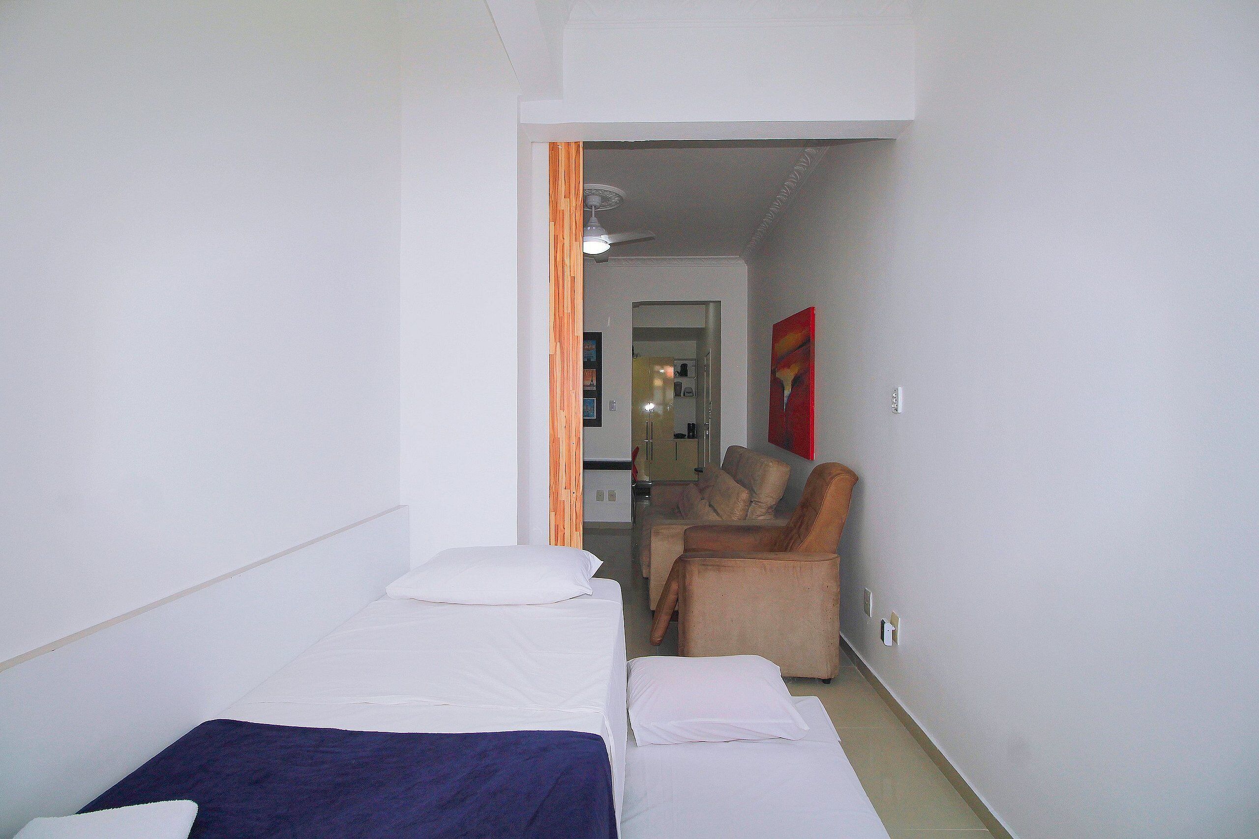 A hotel room with a bed, a chair, and a kitchenette in the background.