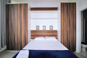 Une chambre d’hôtel avec un grand lit, une armoire en bois et une salle de bain visible à travers une porte ouverte.