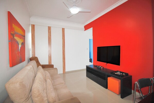 Un salon moderne avec un canapé beige, un meuble de rangement noir et un mur d’accent rouge.