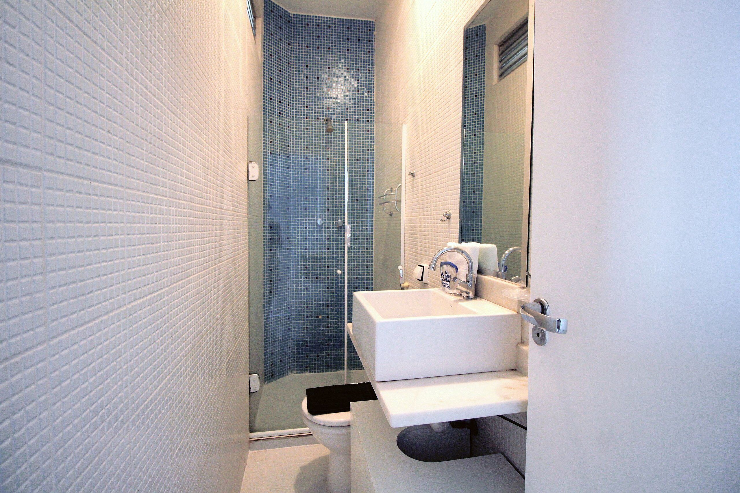 A bathroom with a white sink, a mirror, and a shower with blue mosaic tiles.