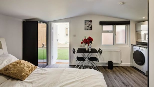 Ein Schlafzimmer mit Bett, Tisch mit Stühlen, Heizkörper und Waschmaschine.