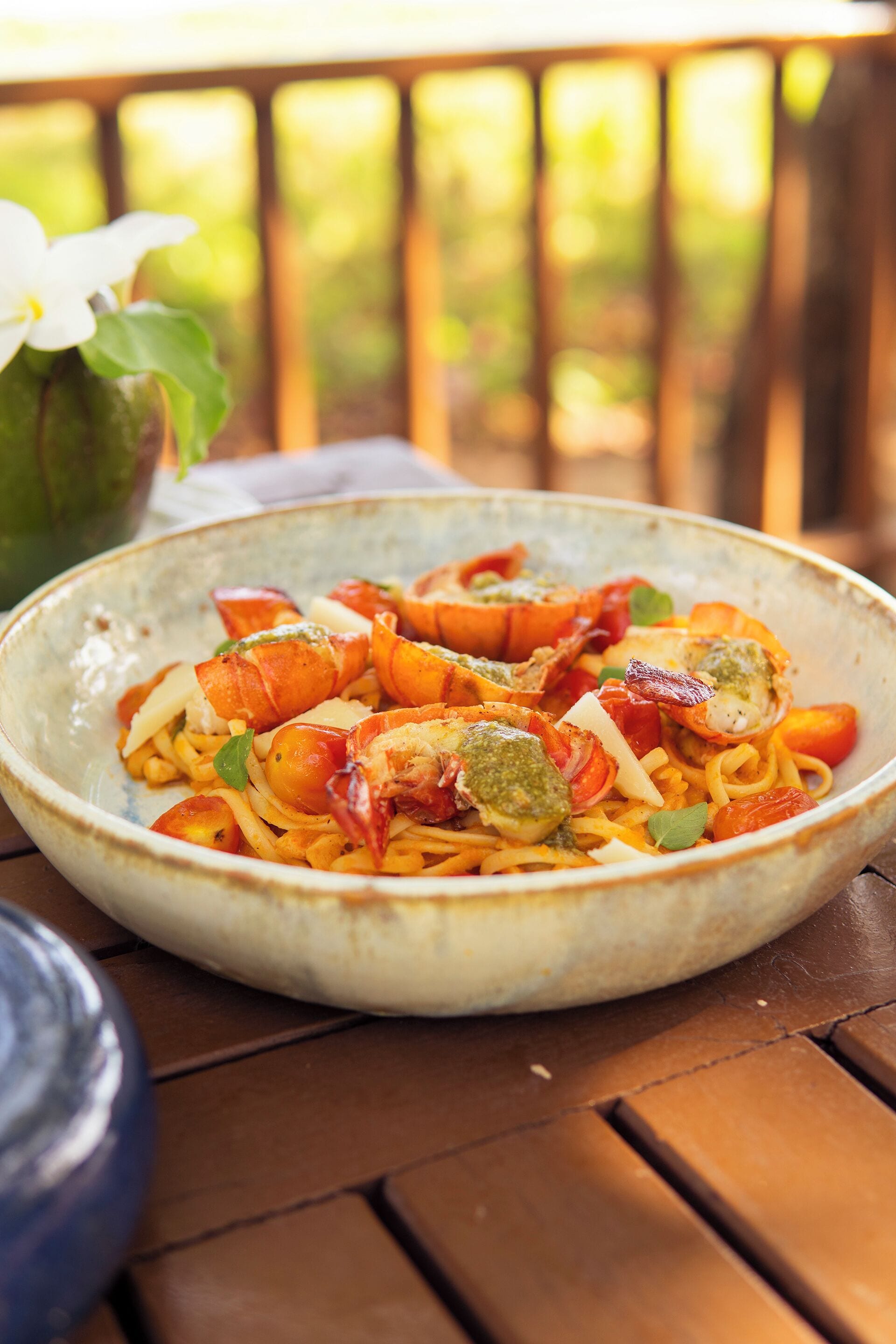 A bowl of pasta with shrimp and vegetables on a wooden table.