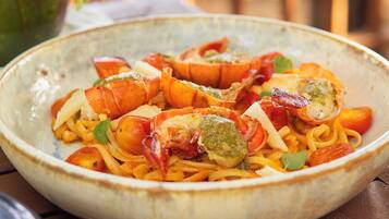 A bowl of pasta with shrimp and vegetables on a wooden table.